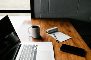 木の机の上に置いたノートパソコン、コーヒーの入ったマグカップ、メモとペン、スマートフォン
